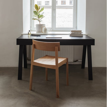 Black home office desk with a wooden chair in a room with a window and plant.