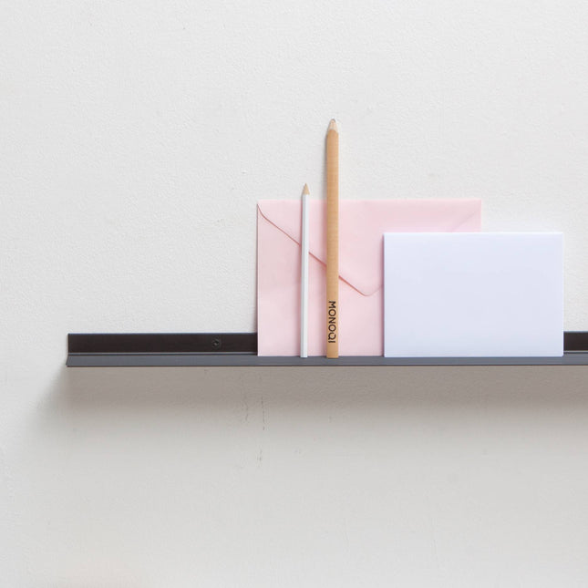 Minimalist metal black frame shelf holding pink, white, and gold stationery items on a light gray background.