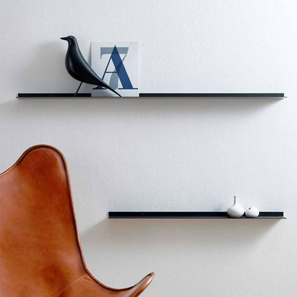 Modern black frame shelf in a minimalist interior with a brown chair, black shelves, and decorative items on a white wall.