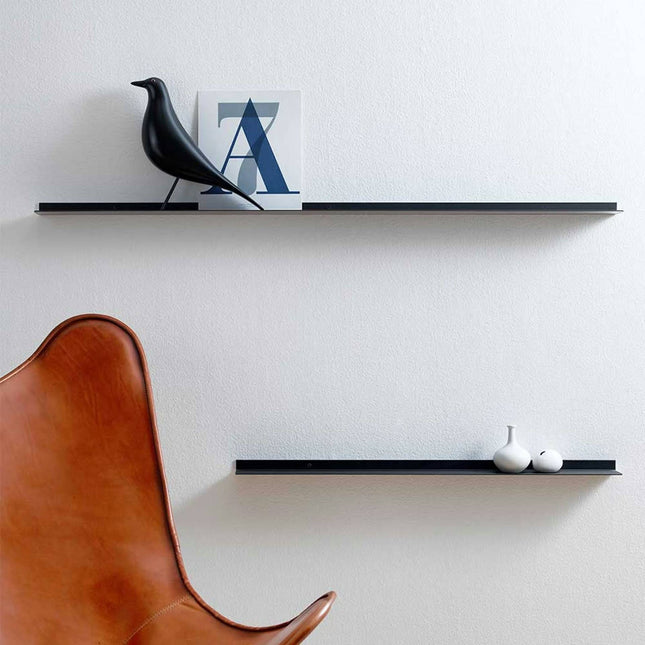 Modern black frame shelf in a minimalist interior with a brown chair, black shelves, and decorative items on a white wall.