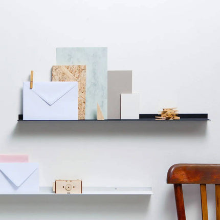 Wall mounted metal frame Shelves with various items including envelopes and a camera against a white wall.