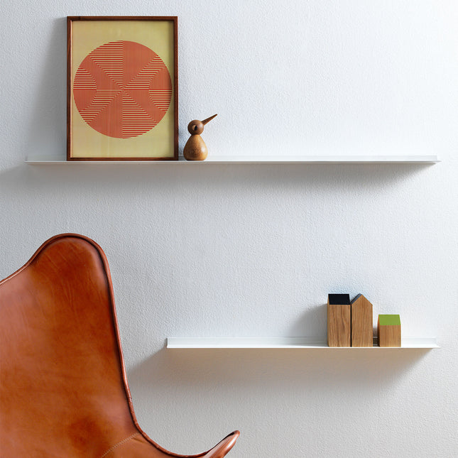 Modern interior with a brown leather chair, white shelves, and decorative items sitting on a white metal frame shelf against a light grey wall.