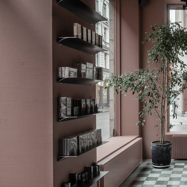 Metal Shelving with books and decor against a pink wall with a plant in the foreground in a commercial environment 