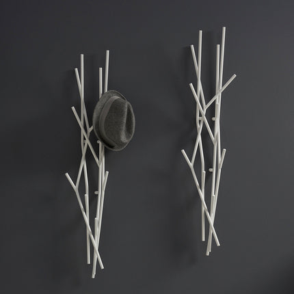 Wall-mounted metal branch-like coat rack with a hat on a dark background