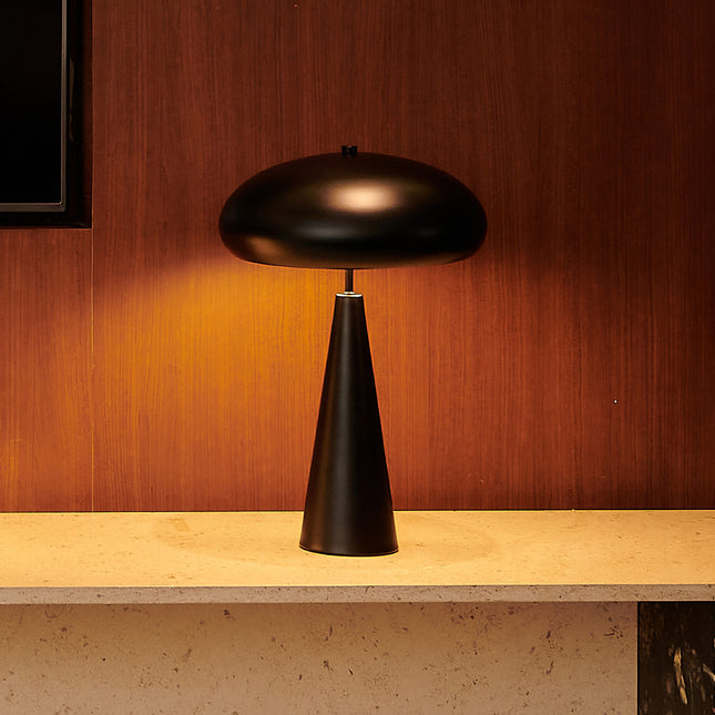 Black mid-century table lamp on a wooden surface with a warm brown background