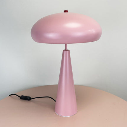 Pink mid-century table lamp on a beige surface with a light gray background