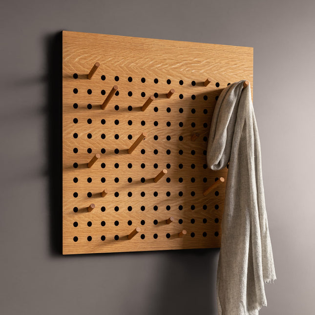 Wooden pegboard with hooks on a wall, holding a gray garment.
