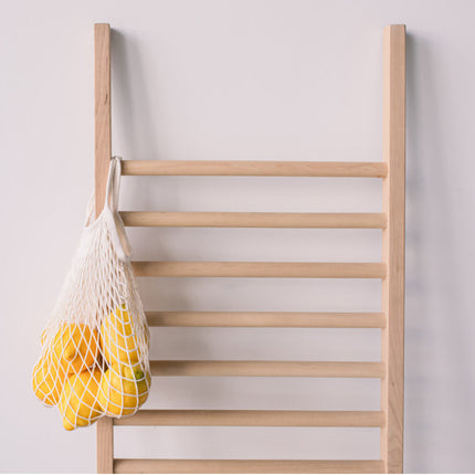 Shoe and Clothes rack in a wooden ladder shape with a net bag of lemons against a light background