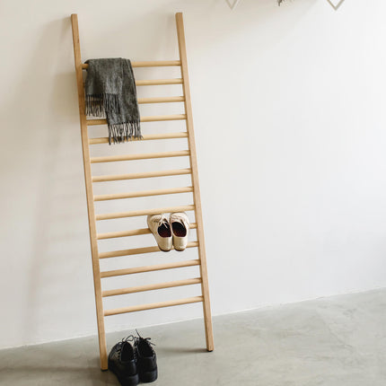 Wooden ladder shoe rack with shoes and a scarf against a white wall