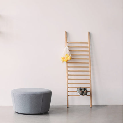 Solid wood ladder clothes rack with decorative items against a white wall, next to a gray ottoman.