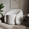 Modern white armchair in a stylish room with a plant and abstract art on the wall.