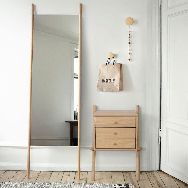 Wooden oak side table against a white wall with a decorative bag hanging on the wall.