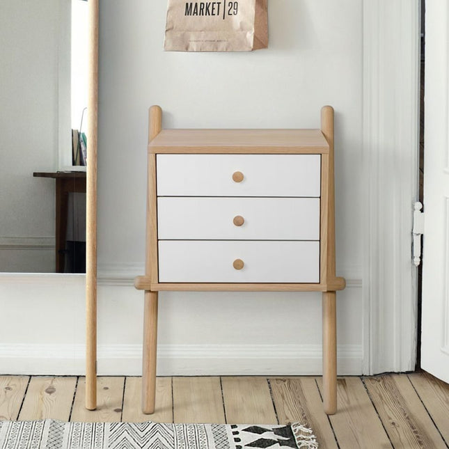Wooden side table with three white drawers in a room with a mirror and rug.